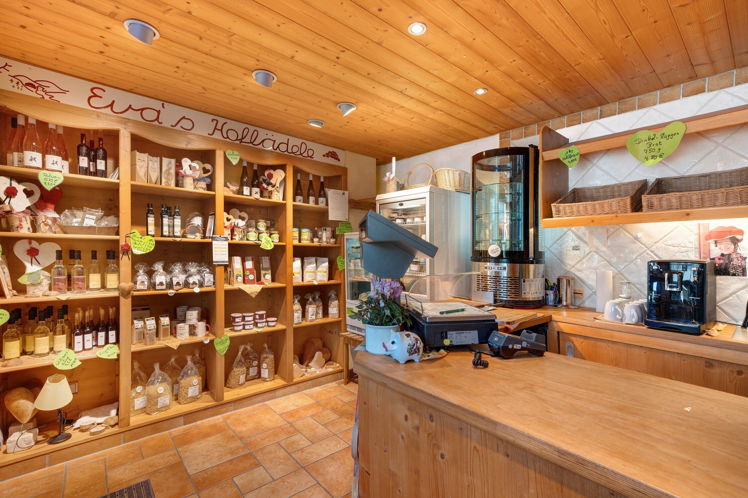 A wooden interior with shelves of bottles and jars, a counter with a coffee machine, and a sign reading 'Eva's Holcadel.'