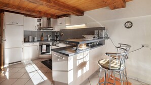 A kitchen with white cabinets, a wooden ceiling, and a bar area with metal chairs. - Holiday Apartment in Farmhouse with Event Room – 3 Apartments in One (Hornberg)