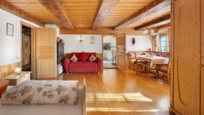 A spacious room with wooden beams on the ceiling, a red sofa, a dining table with chairs, and a wooden cabinet. - Holiday Apartment in Farmhouse with Event Room – 3 Apartments in One (Hornberg)
