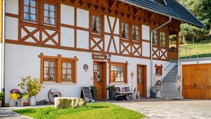 A traditional half-timbered building with a sign reading 'Evas Hofstalle,' a paved courtyard, and a staircase leading to a wooden door. - Holiday Apartment in Farmhouse with Event Room – 3 Apartments in One (Hornberg)