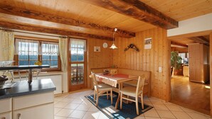 A wooden interior with a dining table, chairs, a kitchen area, and a view through a window. - Holiday Apartment in Farmhouse with Event Room – 3 Apartments in One (Hornberg)