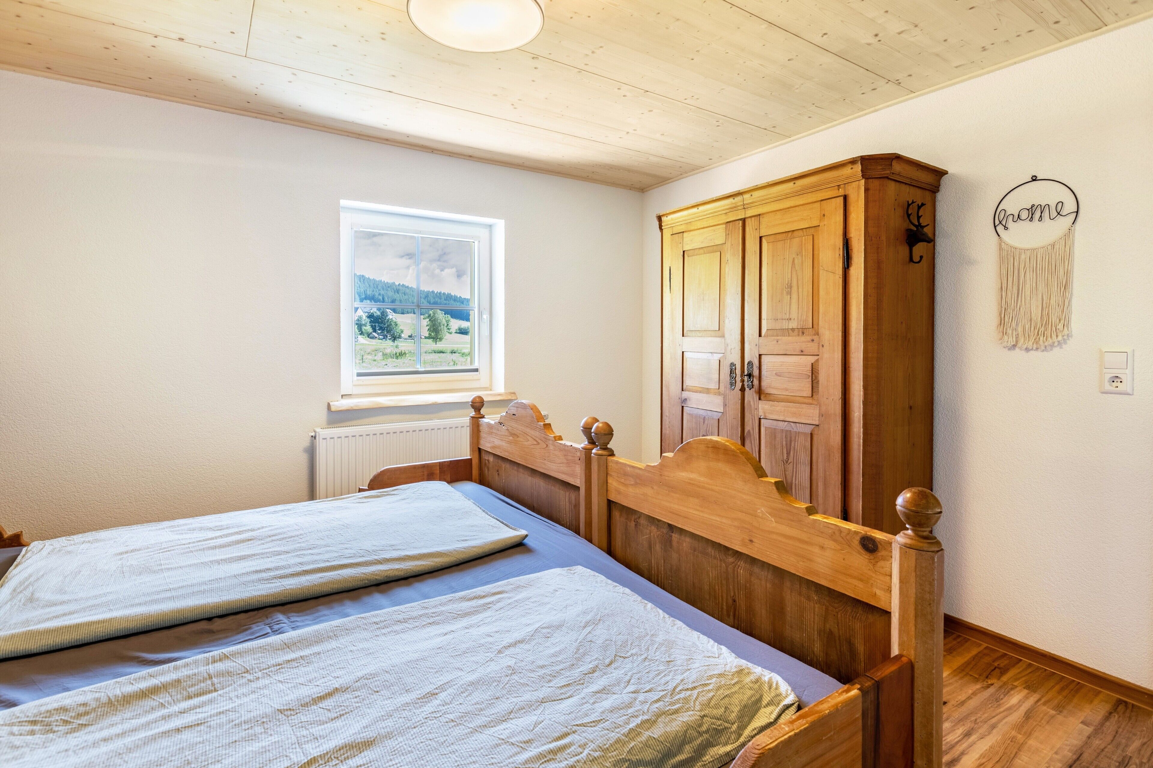 Een slaapkamer met twee houten bedden, een raam met uitzicht, een houten kledingkast en een wanddecoratie.