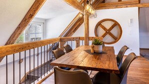 A wooden dining table with chairs, a hanging light fixture, and a large wooden beam structure. - Mühlen Chalet Apartment with Private Terrace (Titisee-Neustadt)