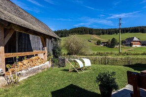 Une grange rustique avec un toit de chaume, une pile de bois de chauffage et une clôture en bois.