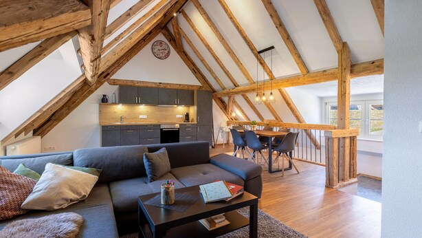 A loft-style living space with a dining area, wooden beams, and a kitchen. - Mühlen Chalet Apartment with Private Terrace (Titisee-Neustadt)