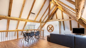 A loft-style room with exposed wooden beams, a dining area with chairs and a table, a sofa, and a television. - Mühlen Chalet Apartment with Private Terrace (Titisee-Neustadt)