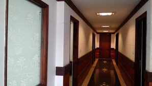 A hotel hallway with a carpeted floor, wooden doors, and a patterned wall on the left. - Hotel Sagar By GRB (Meerut)