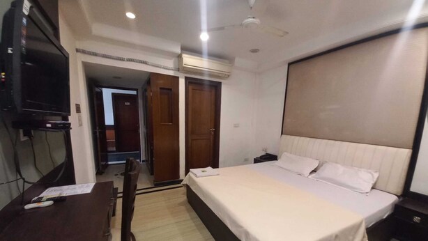 A bedroom with a bed, bedside table, desk, chair, TV, and wardrobe. - Hotel Sagar By GRB (Meerut)