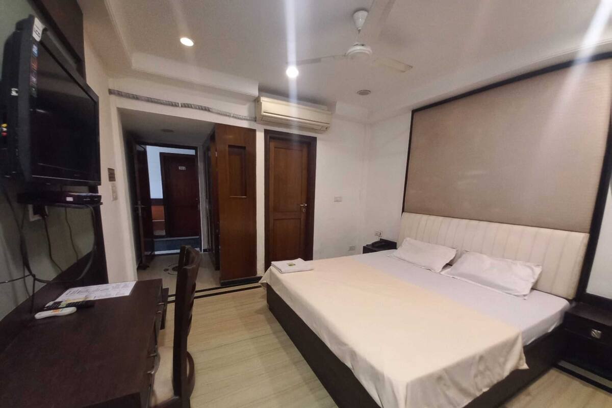 A bedroom with a bed, bedside table, desk, chair, TV, and wardrobe.