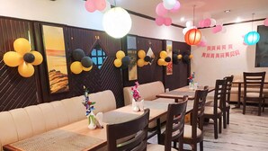 A restaurant with a modern interior, featuring a long dining table with chairs, cushioned seating, and decorative balloons. - Hotel Sagar By GRB (Meerut)