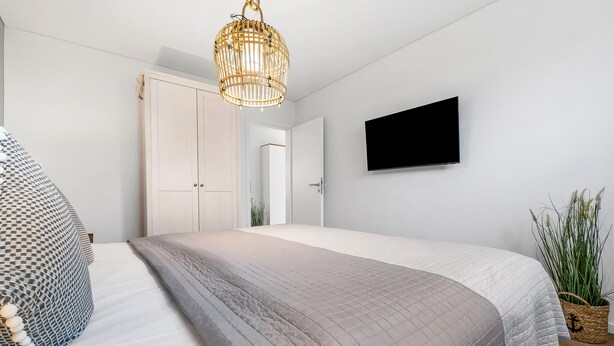 Ein Schlafzimmer mit einem Bett, einem Fernseher, einer Tür und einer Hängeleuchte.