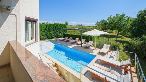 Ein Pool auf dem Dach mit Liegestühlen und Sonnenschirmen, umgeben von Grünpflanzen und blauem Himmel.