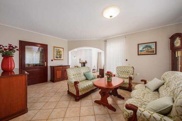 A living room with a wooden coffee table, two patterned armchairs, a sofa, a wooden cabinet, and a door with a glass panel.