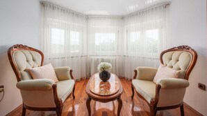 Ein Zimmer mit zwei verzierten Stühlen, die einem runden Holztisch mit Blumenvase gegenüberliegen.