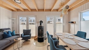 En moderne stue med sofa, stole, spisebord, pejs og store vinduer.