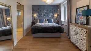 A bedroom with a large bed, bedside tables, a dresser, a mirror, and a wall with a floral pattern. - Ker Lan - Character house with Spa and sea view (Lanildut)