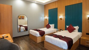 Une chambre d’hôtel avec deux lits, un plancher en bois, un ventilateur de plafond, un miroir et une petite table avec une chaise.