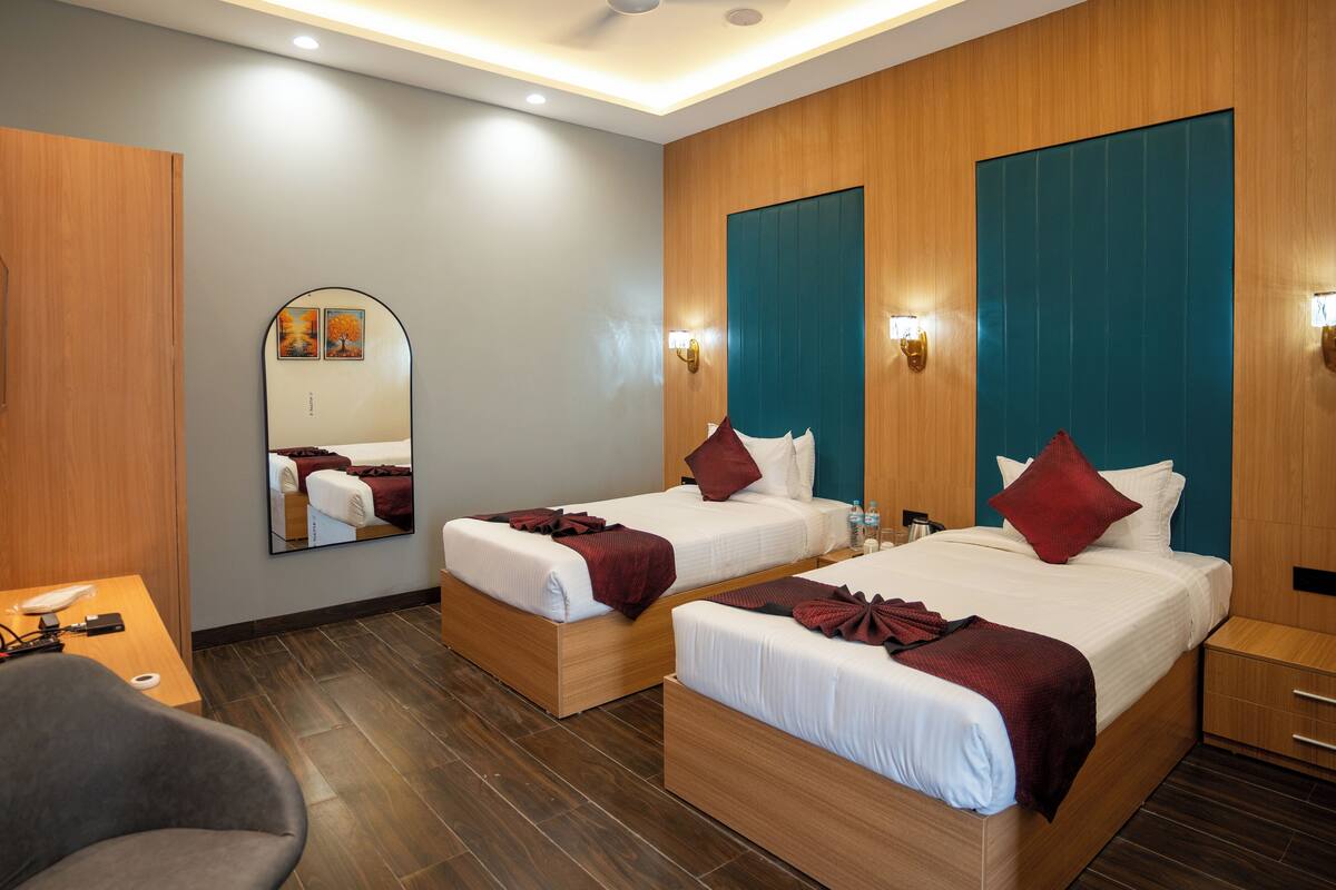 A hotel room with two beds, wooden flooring, a ceiling fan, a mirror, and a small table with a chair.