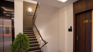 Un intérieur moderne avec un escalier, une porte en bois portant l’inscription « 101 », et une plante en pot.