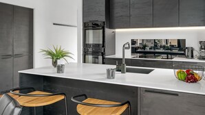 A modern kitchen with a central island, two bar stools, a sink, and a built-in oven.