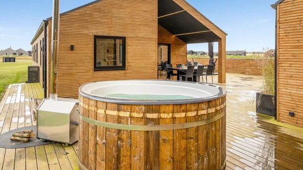A wooden cabin with a hot tub, outdoor seating, and a chimney.