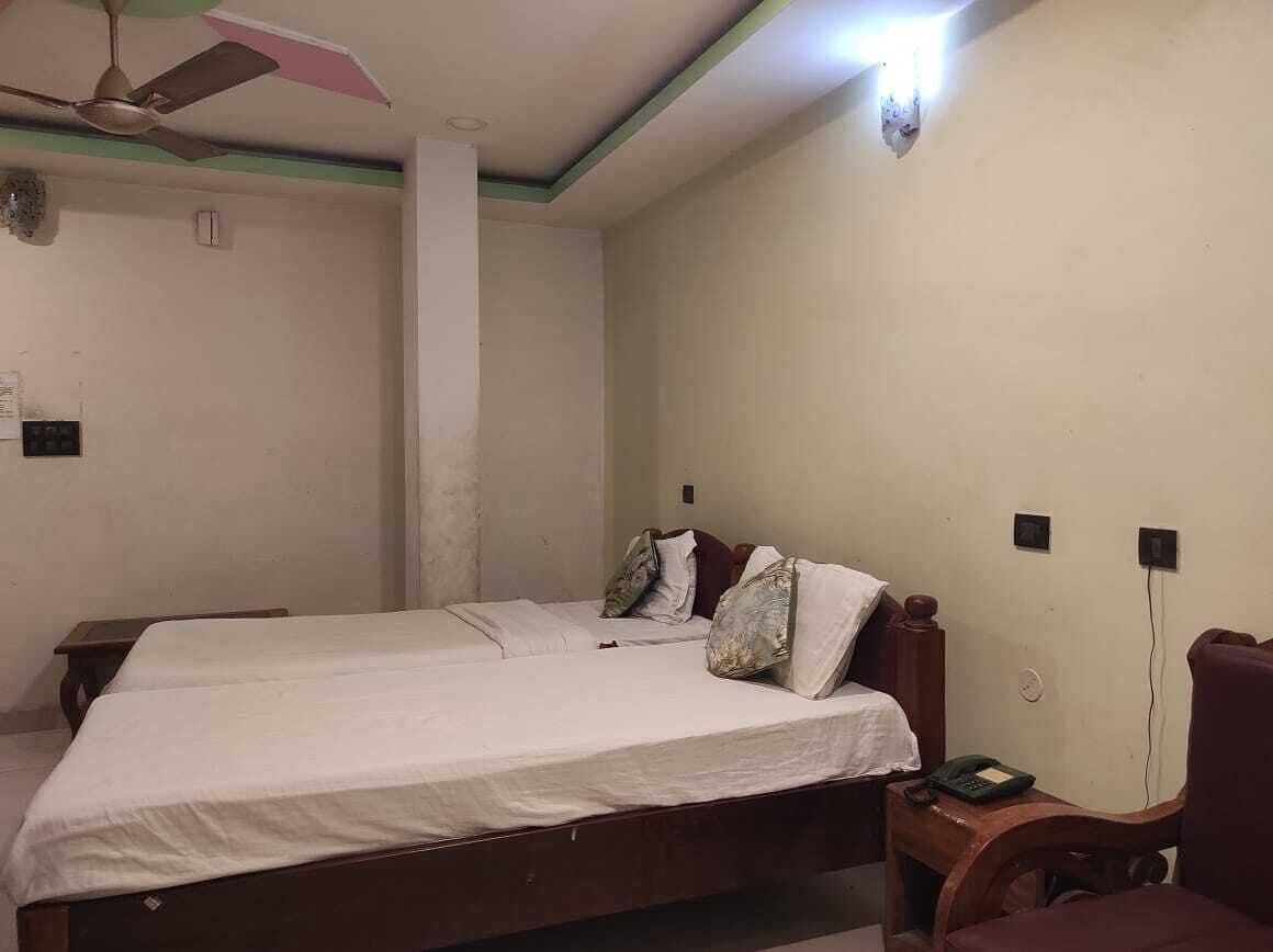 Una habitación con dos camas individuales, un ventilador de techo, una lámpara de pared y un teléfono sobre una mesa de madera.