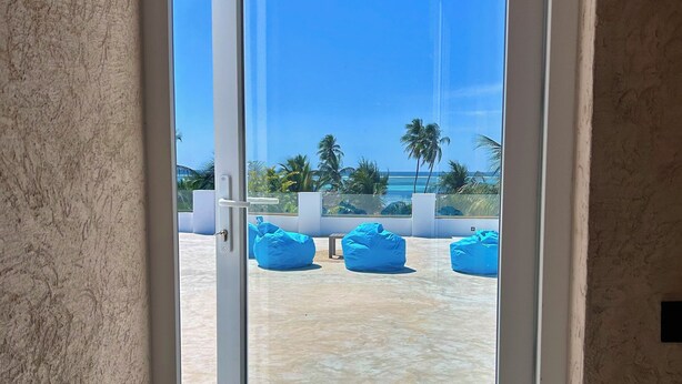 Una puerta con vista a una playa, con sillones azules tipo bean bag y palmeras.