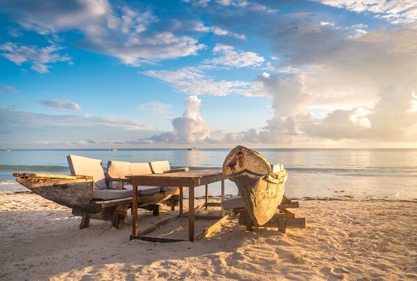 A beach with a wooden table and chairs, a large wooden bucket, and a calm sea in the background. - Private Pool Villa Kokos (Kiwengwa)