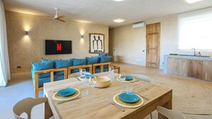 A modern kitchen with wooden cabinets, a dining table set for four, and a television mounted on the wall. - Private Pool Villa Kokos (Kiwengwa)