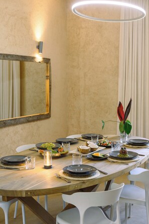 A dining area with a round table set for a meal, surrounded by white chairs. - Private Pool Villa Kokos (Kiwengwa)