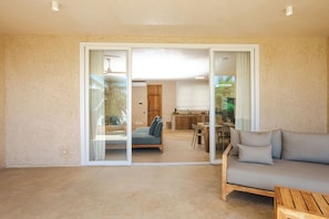 A spacious living area with a sliding glass door leading to a balcony, a sofa, a wooden table, and a kitchen area with a dining table and chairs. - Private Pool Villa Kokos (Kiwengwa)