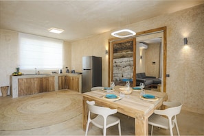 A modern kitchen with a dining area, wooden cabinets, a large window, and a stone wall.