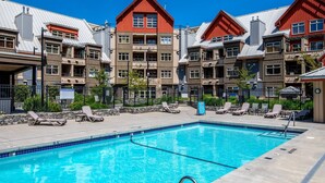 A swimming pool with lounge chairs and a stone wall. - Lake Placid Lodge Loft 2 bedroom (Whistler)
