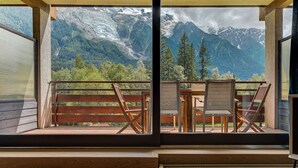 A balcony with a view of snow-capped mountains, wooden furniture, and a wooden railing.