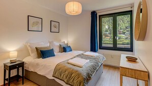 A bedroom with a bed, bedside tables, a desk, a window with a view, and a hanging light fixture.