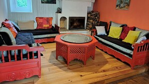 A cozy living room with a fireplace, two sofas, a coffee table, and a window with blinds. - Maison de Campagne Proche Monts D'ambazac et Limoges (La Jonchère-Saint-Maurice)