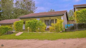 A row of single-story buildings with tiled roofs, surrounded by greenery and a dirt path. - Riverside Villas Nanyuki  (Nanyuki)
