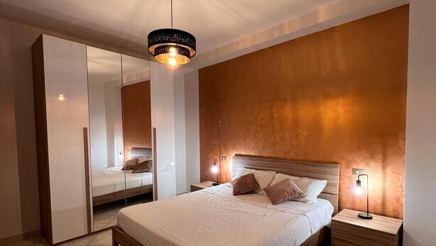 Une chambre à coucher moderne avec un grand lit, une armoire, une table de chevet et une lampe suspendue.