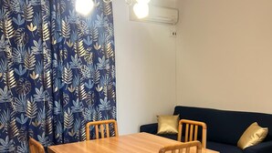 Un coin repas avec une table en bois et quatre chaises, un canapé bleu avec des coussins dorés et un rideau à motifs.