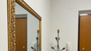 Un couloir avec un miroir encadré d’or, un banc en bois foncé, une porte et un luminaire fixé au mur.