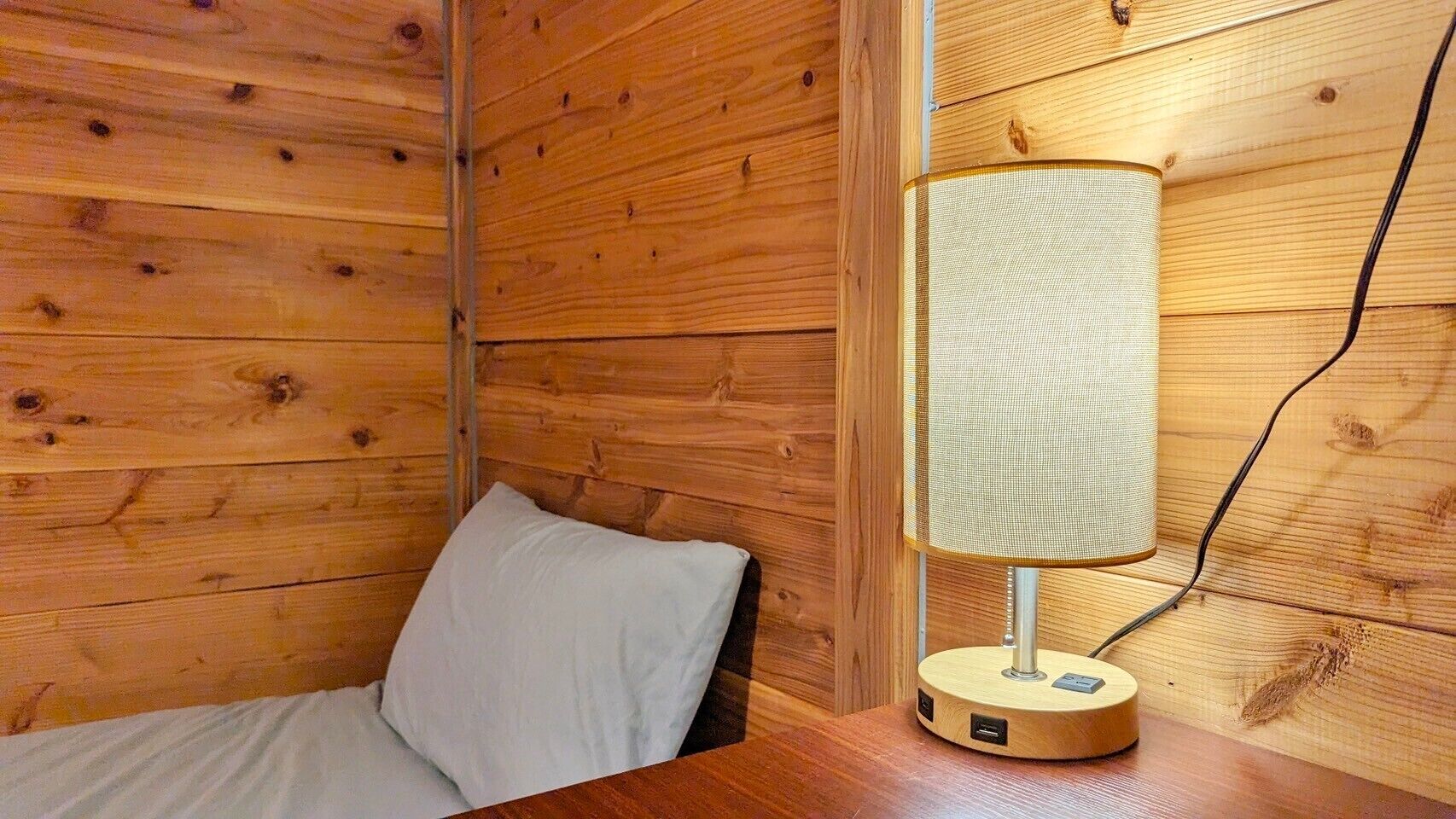 Une pièce de cabane en bois comprenant un lit, une lampe fixée au mur et une prise de courant.