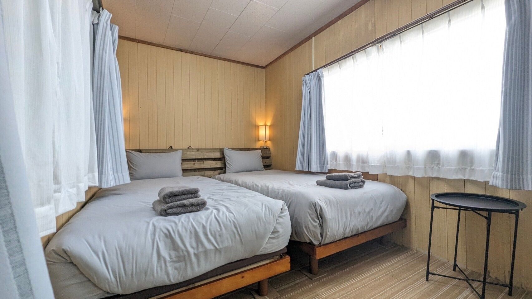 A room with two beds, a small table, and a window with curtains.