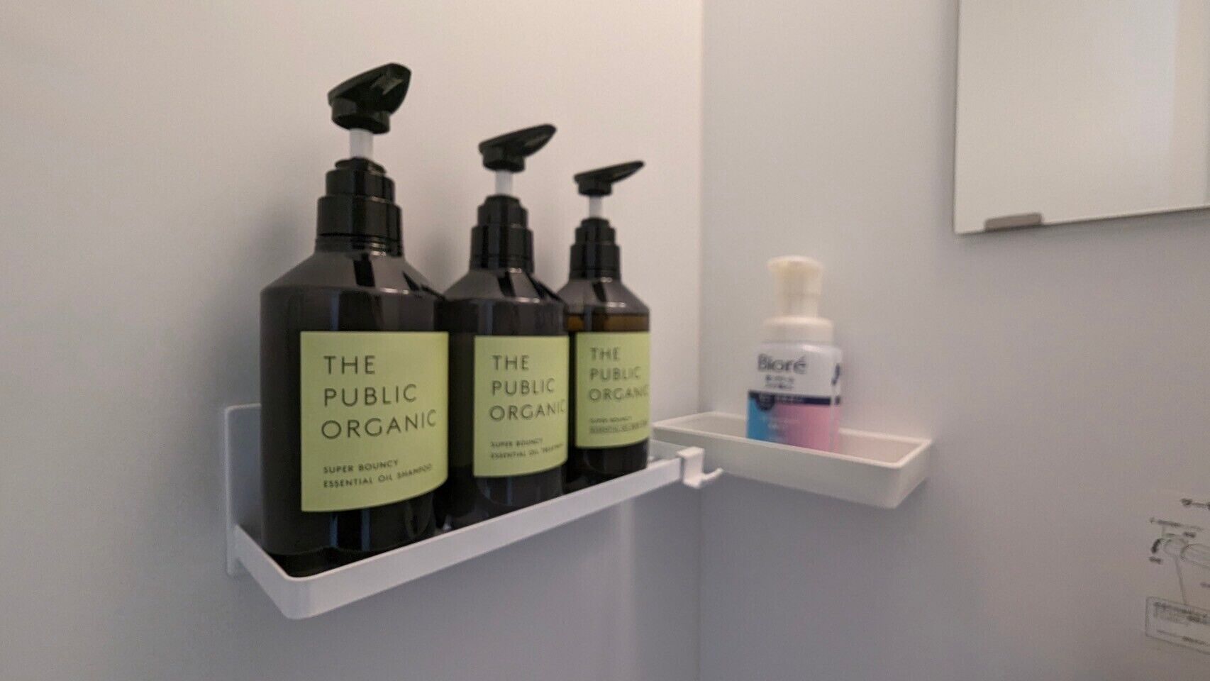 Un estante en el baño con tres botellas de champú de aceites esenciales 'The Public Organic' y una botella de Biore.