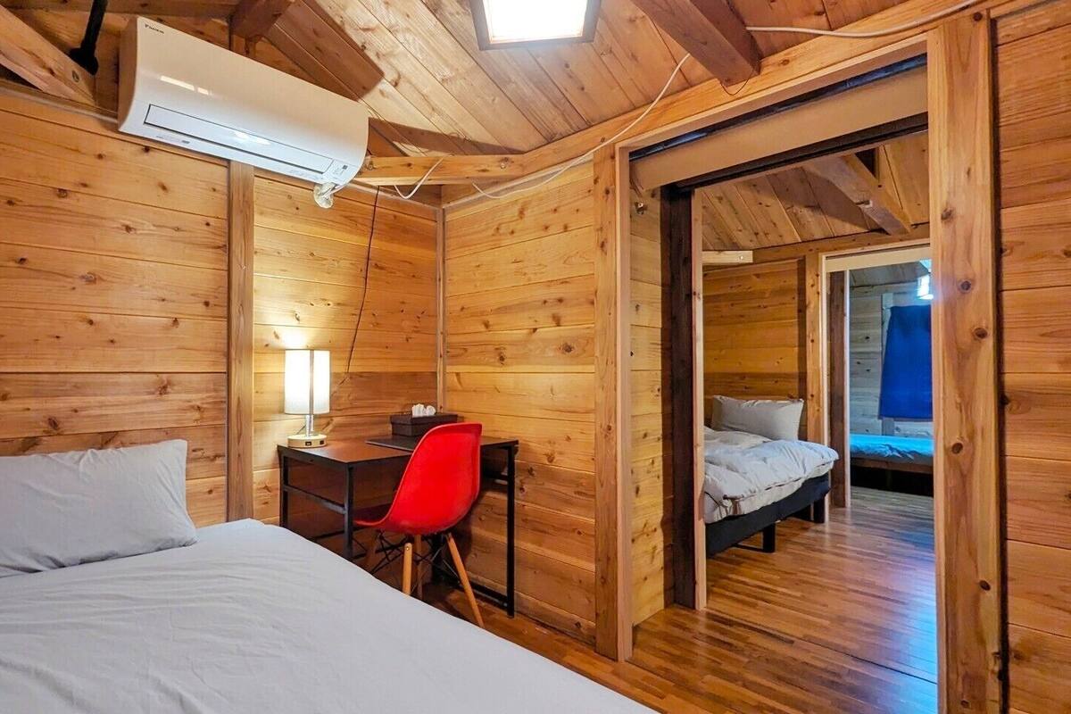 Ein Zimmer in einer Holzhütte mit einem Bett, einem Schreibtisch mit Lampe und einem roten Sessel.