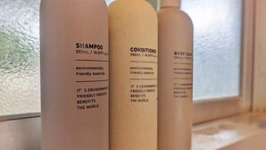 Tres botellas de champú, acondicionador y jabón corporal con etiquetas que indican materiales ecológicos y beneficios para el planeta.