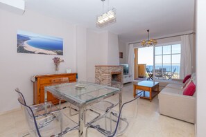 Un salon moderne avec une table à manger en verre, une cheminée, un canapé offrant une belle vue et un balcon avec une table et des chaises.