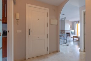 Un couloir mène à une salle à manger avec une cheminée, et on aperçoit une cuisine au fond. Une porte avec un téléphone fixé au mur se trouve également dans le couloir.
