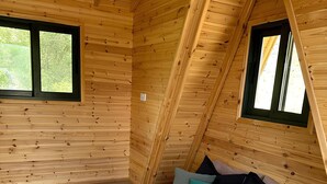 Een houten kamer met een bed, twee ramen en een schuine kap.