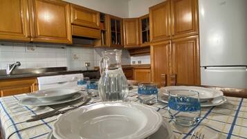 Una cucina con mobili in legno, un frigorifero bianco e un tavolo da pranzo apparecchiato con piatti, bicchieri e posate.
