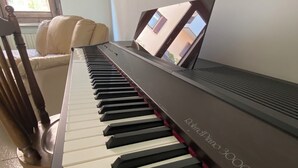 Een piano met een digitaal scherm in een kamer, met een stoel en een raam.